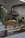 A bakery counter displays a variety of freshly baked pastries, including croissants and loaves of bread. In the background, there are industrial kitchen elements like a metal ventilation hood. A vase with white flowers and catkins decorates the counter, adding a touch of elegance.
