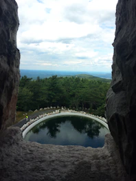 Handcrafted stone pool surrounded by lush greenery under the clear sky in a mountain valley.