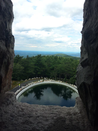 Handcrafted stone pool surrounded by lush greenery under the clear sky in a mountain valley.