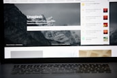 A laptop screen displays the homepage of the Unsplash website. The site features a search bar over an image of a snowy mountain landscape with trees. Notifications appear on the right side of the screen indicating user achievements and updates.