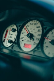 A close-up view of a car dashboard displaying an analog speedometer with measurements in both miles per hour and kilometers per hour. The dashboard is lit with red and white lighting, indicating a partial fuel tank and a digital odometer reading 65279.