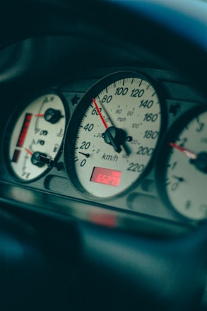 A close-up view of a car dashboard displaying an analog speedometer with measurements in both miles per hour and kilometers per hour. The dashboard is lit with red and white lighting, indicating a partial fuel tank and a digital odometer reading 65279.
