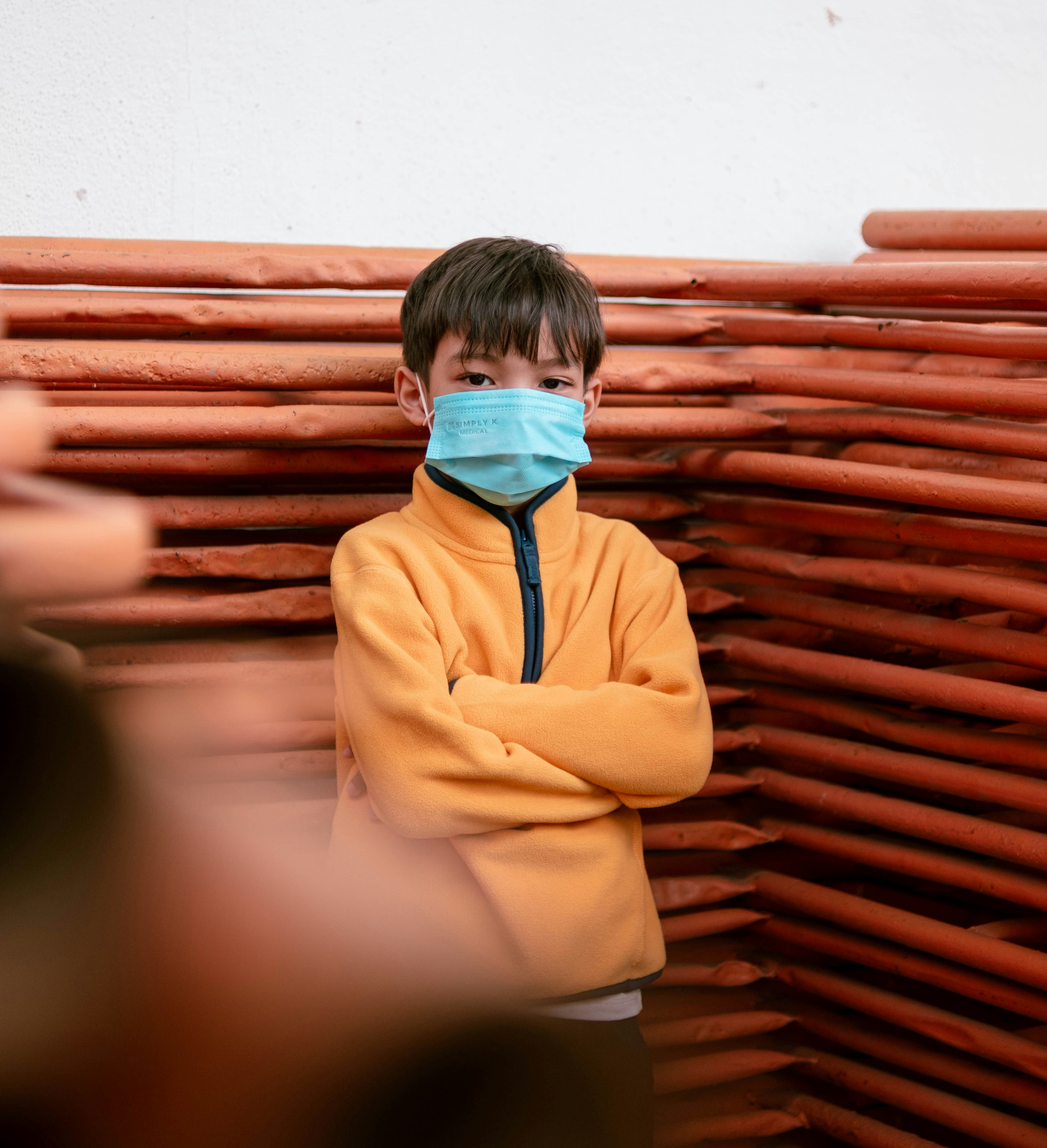 a young boy wearing a face mask while standing in front of a stack of wooden