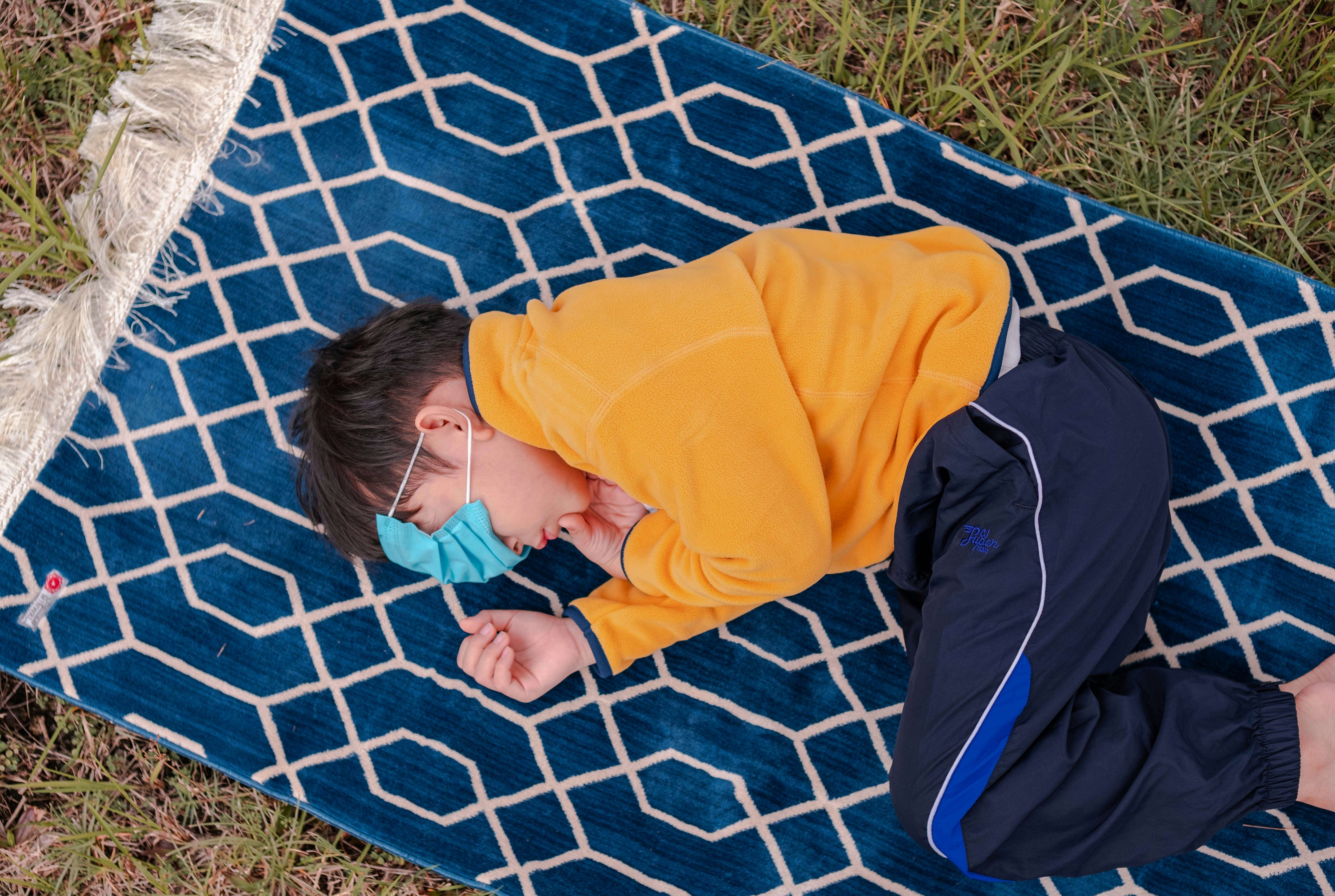 a young boy wearing a face mask laying on a blue rug