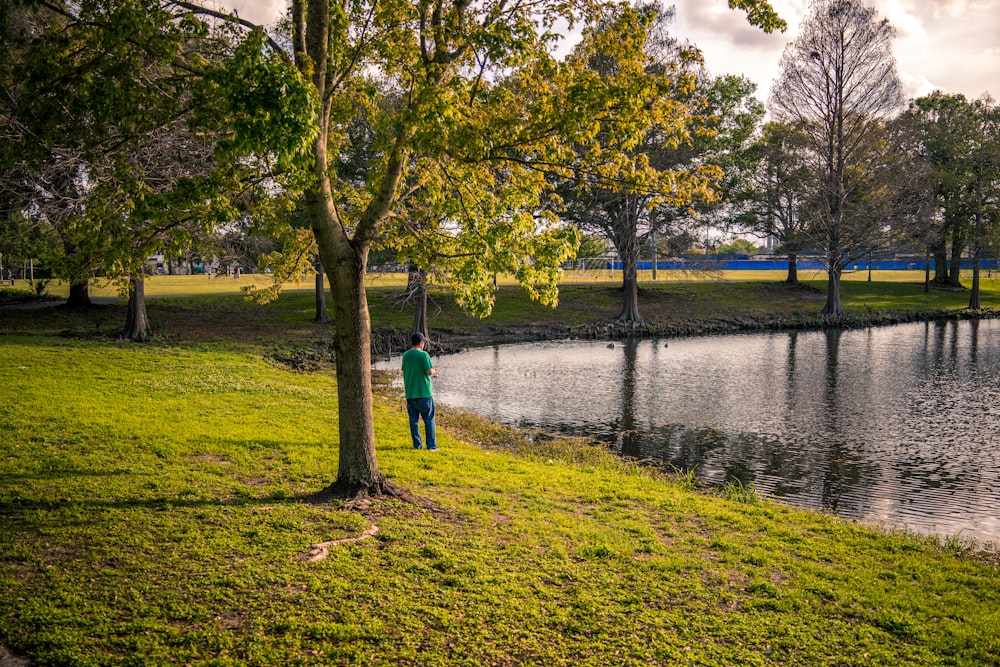 a man standing next to a tree near a lake