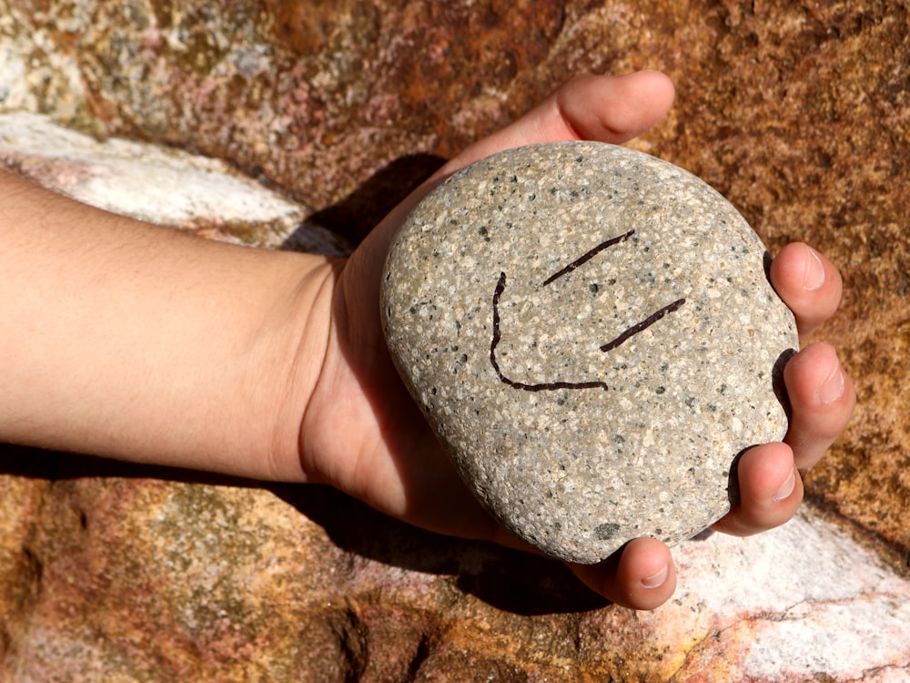 uma mão segurando uma rocha com um rosto sorridente desenhado sobre ela