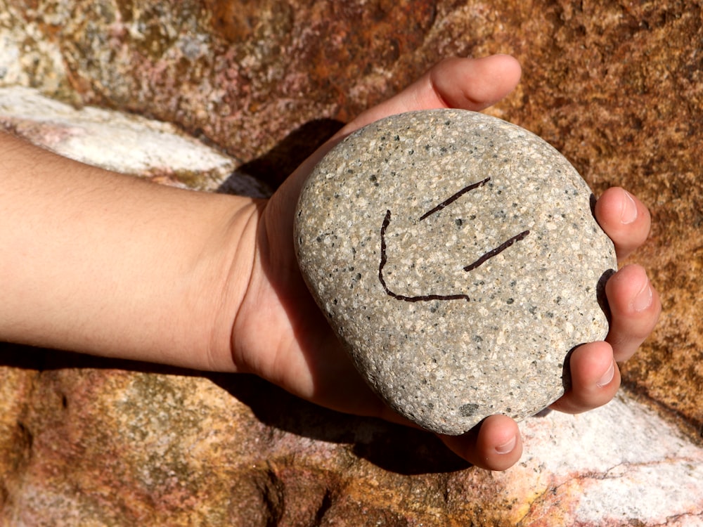 una mano che tiene una roccia con una faccina sorridente disegnata su di essa