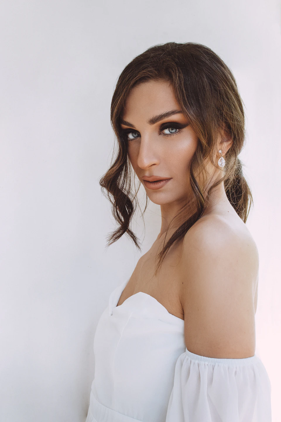 Woman with brown hair and loose waves looks directly at the camera in white dress