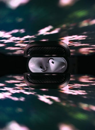 A pair of white wireless earbuds are neatly placed inside a dark charging case. The image features a reflection of the earbuds and case below, with a background displaying colorful, abstract light patterns.