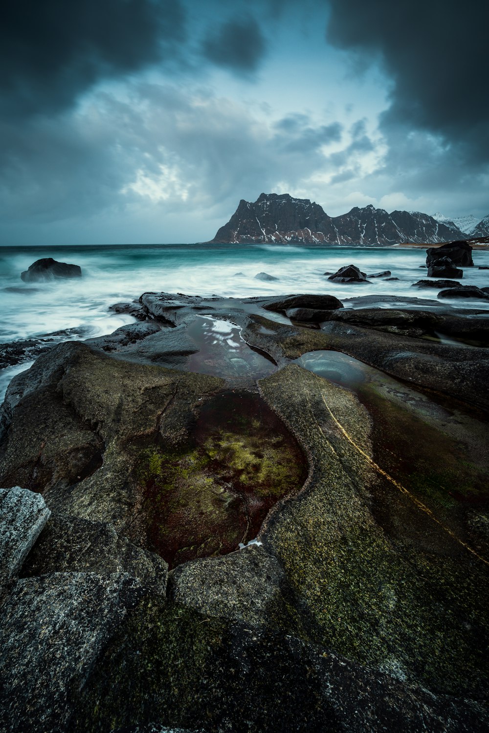 a rocky beach with a body of water and a mountain in the distance