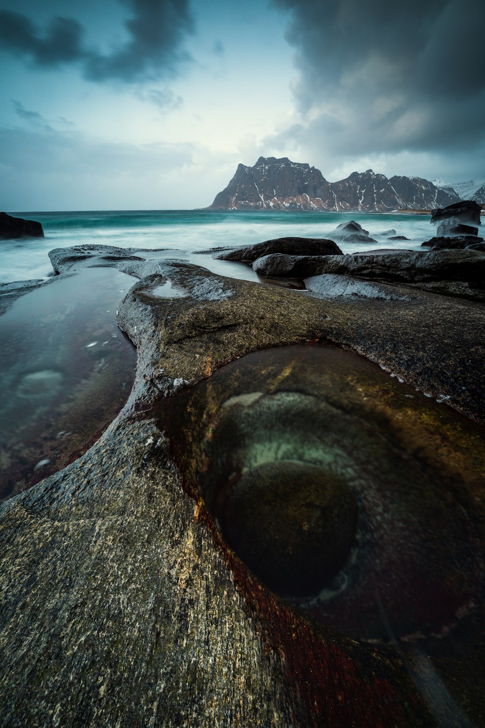 a large rock sitting on top of a beach under a cloudy sky