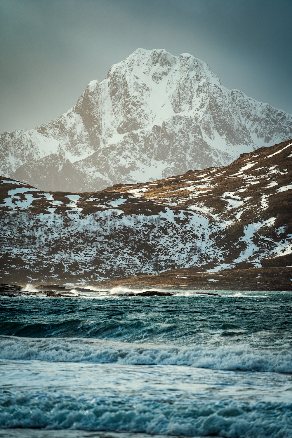 a mountain covered in snow next to a body of water