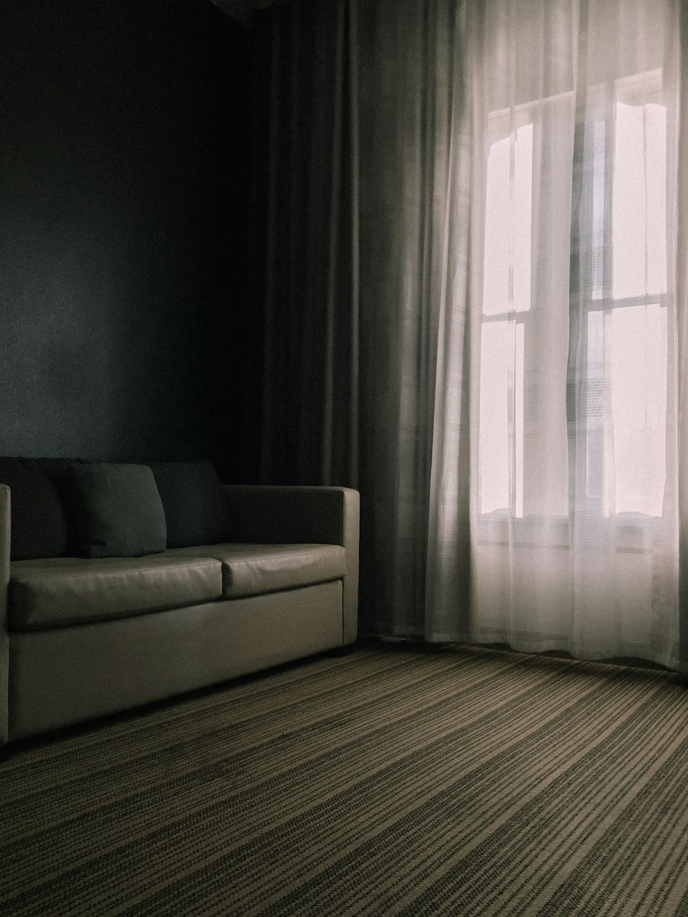 a couch sitting in front of a window next to a curtain