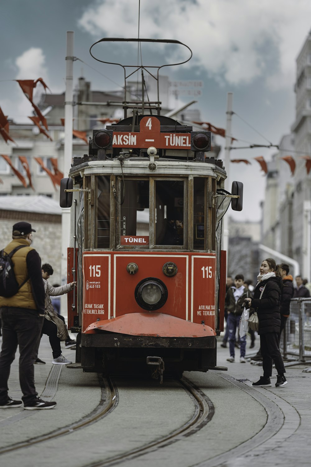 a red trolley car traveling down a street next to a crowd of people