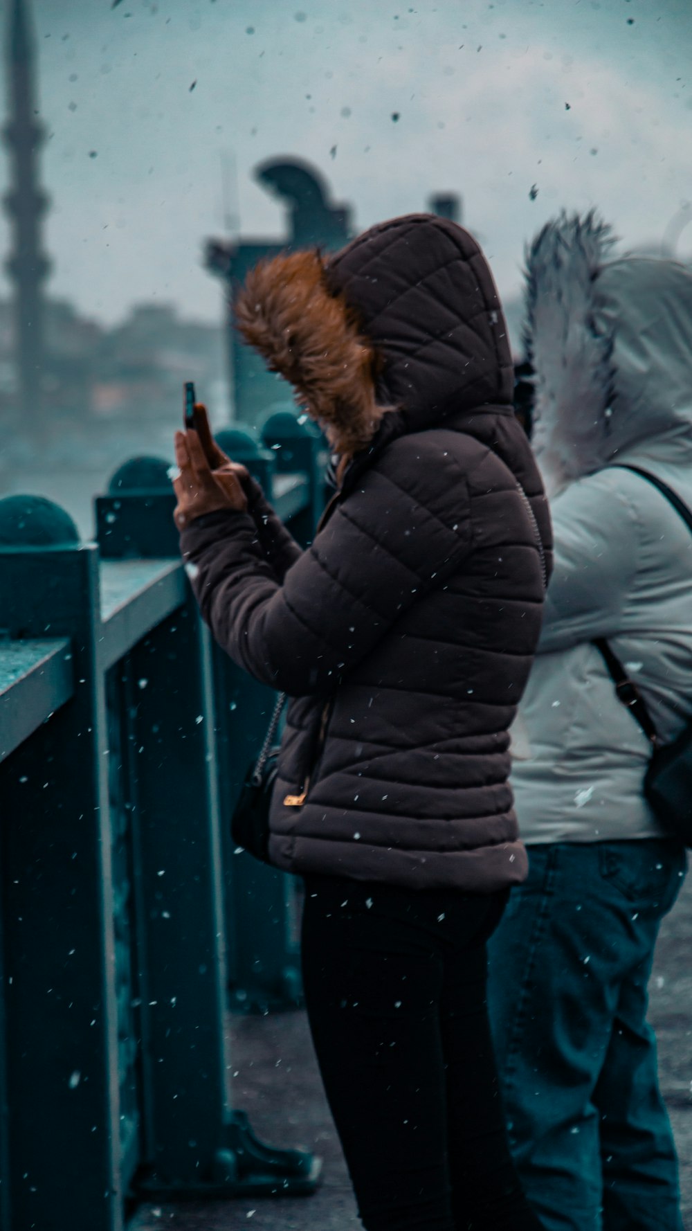 two people standing on a pier looking at their cell phones