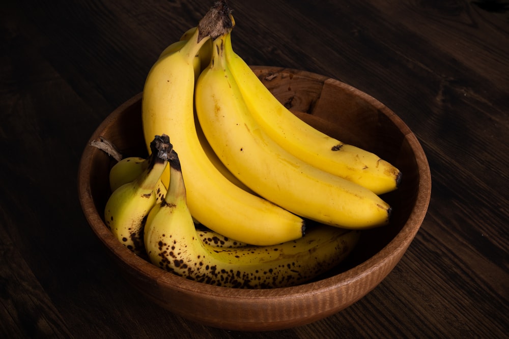 a wooden bowl filled with ripe bananas on top of a wooden table