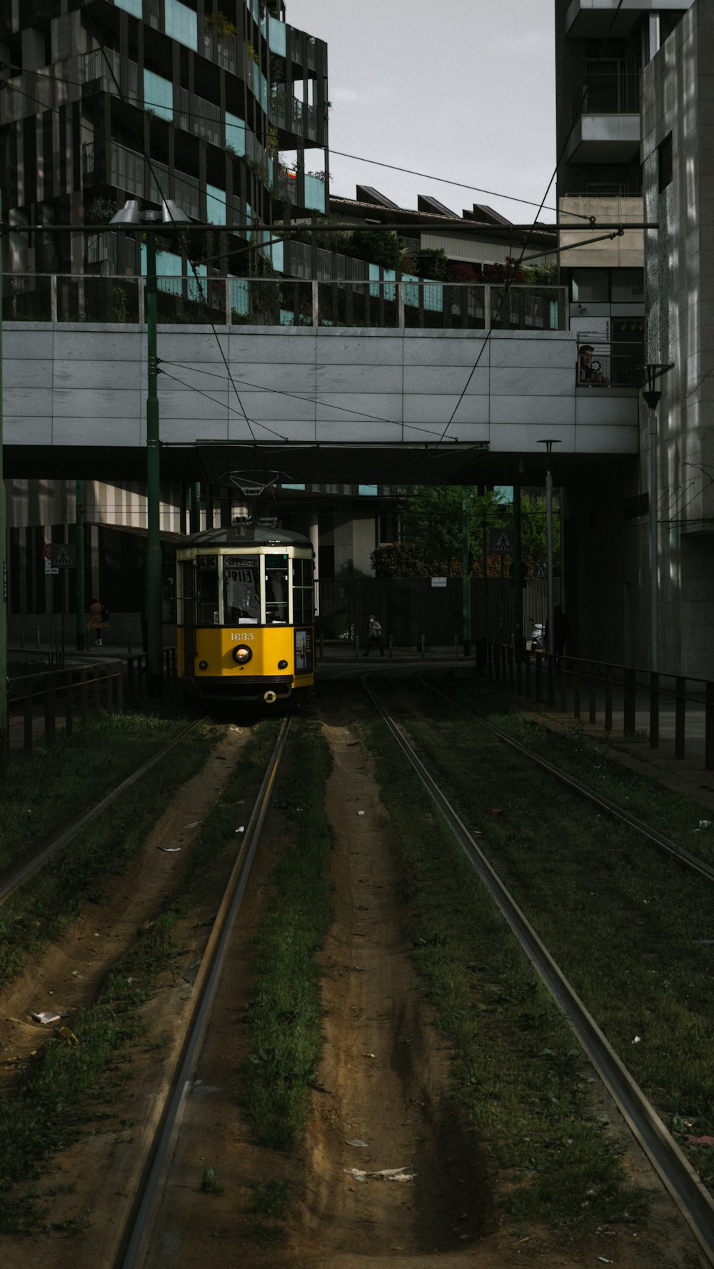 a yellow train traveling down train tracks under a bridge