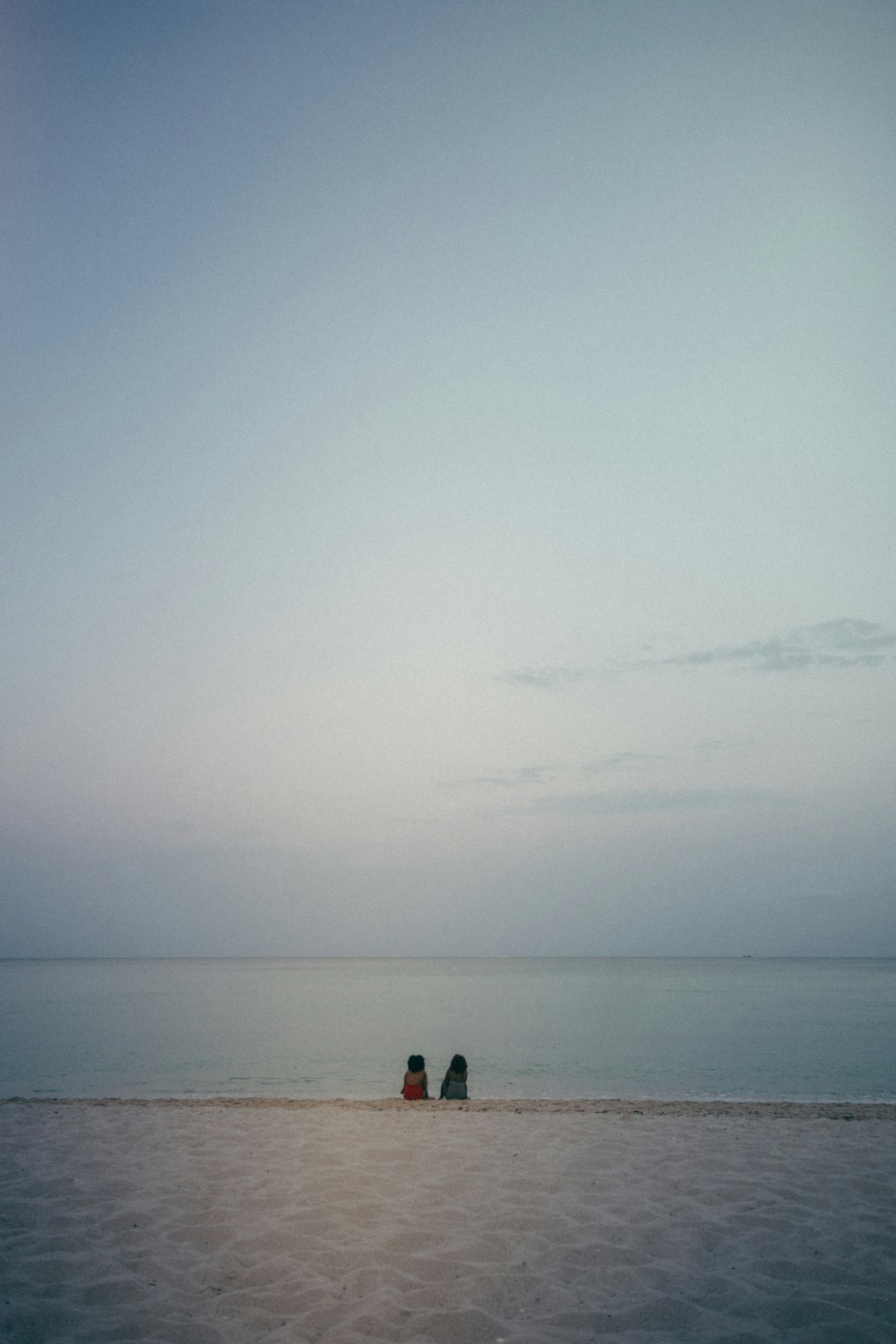 two people sitting on a beach with the ocean in the background
