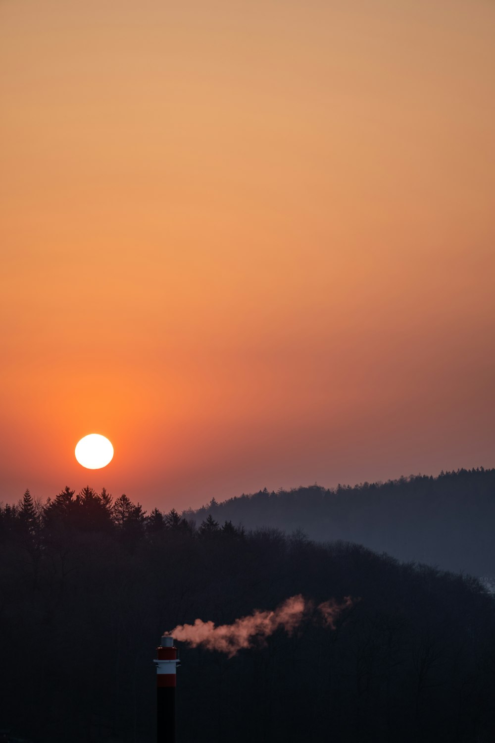 the sun is setting over the mountains with smoke coming out of it