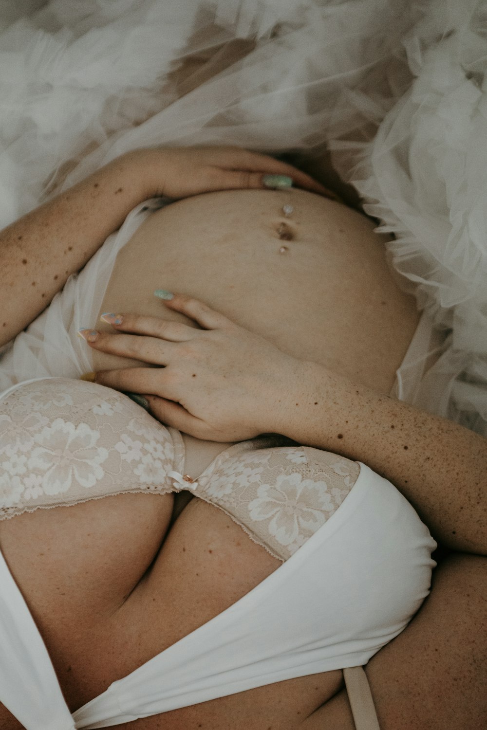 a pregnant woman in a white bra laying on a bed