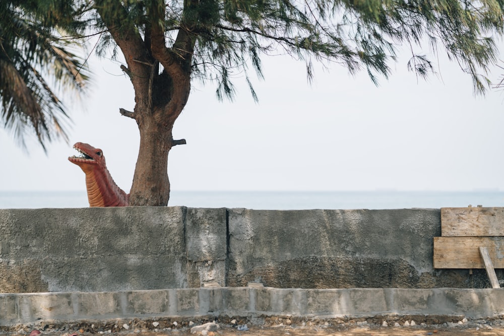 a dinosaur sitting on a concrete wall next to a tree