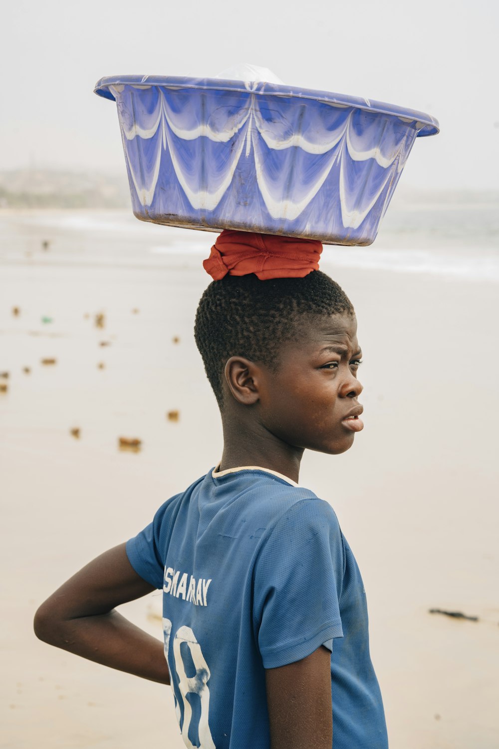 a boy standing on the beach with a bucket on his head