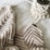 A cozy, knitted blanket with a zigzag pattern is laid out alongside a macrame plant hanger, both positioned on a soft, white fabric surface. The textures are rich and tactile, highlighting intricate craftsmanship.