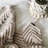 A cozy, knitted blanket with a zigzag pattern is laid out alongside a macrame plant hanger, both positioned on a soft, white fabric surface. The textures are rich and tactile, highlighting intricate craftsmanship.