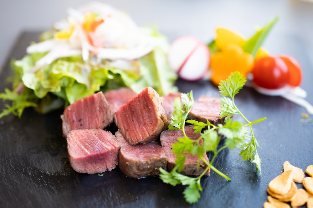 a black cutting board topped with meat and vegetables