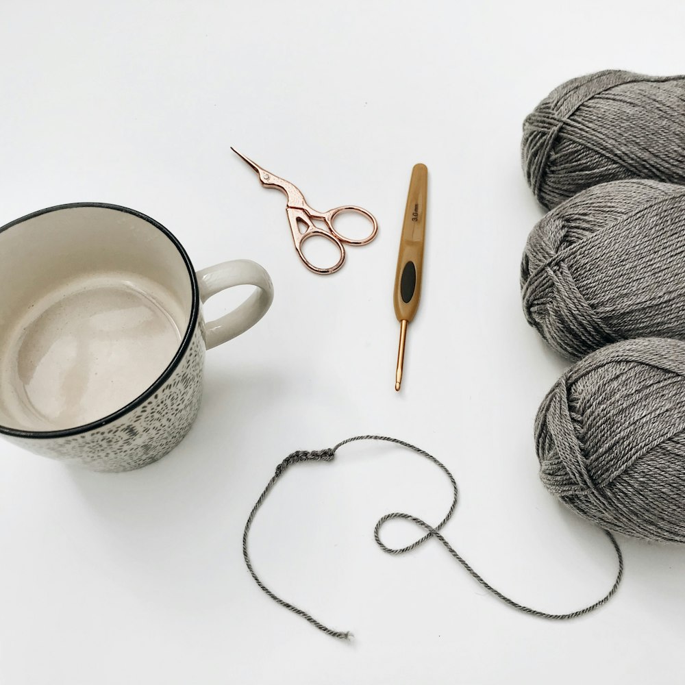 a cup of yarn, a pair of scissors, and a pair of knitting needles