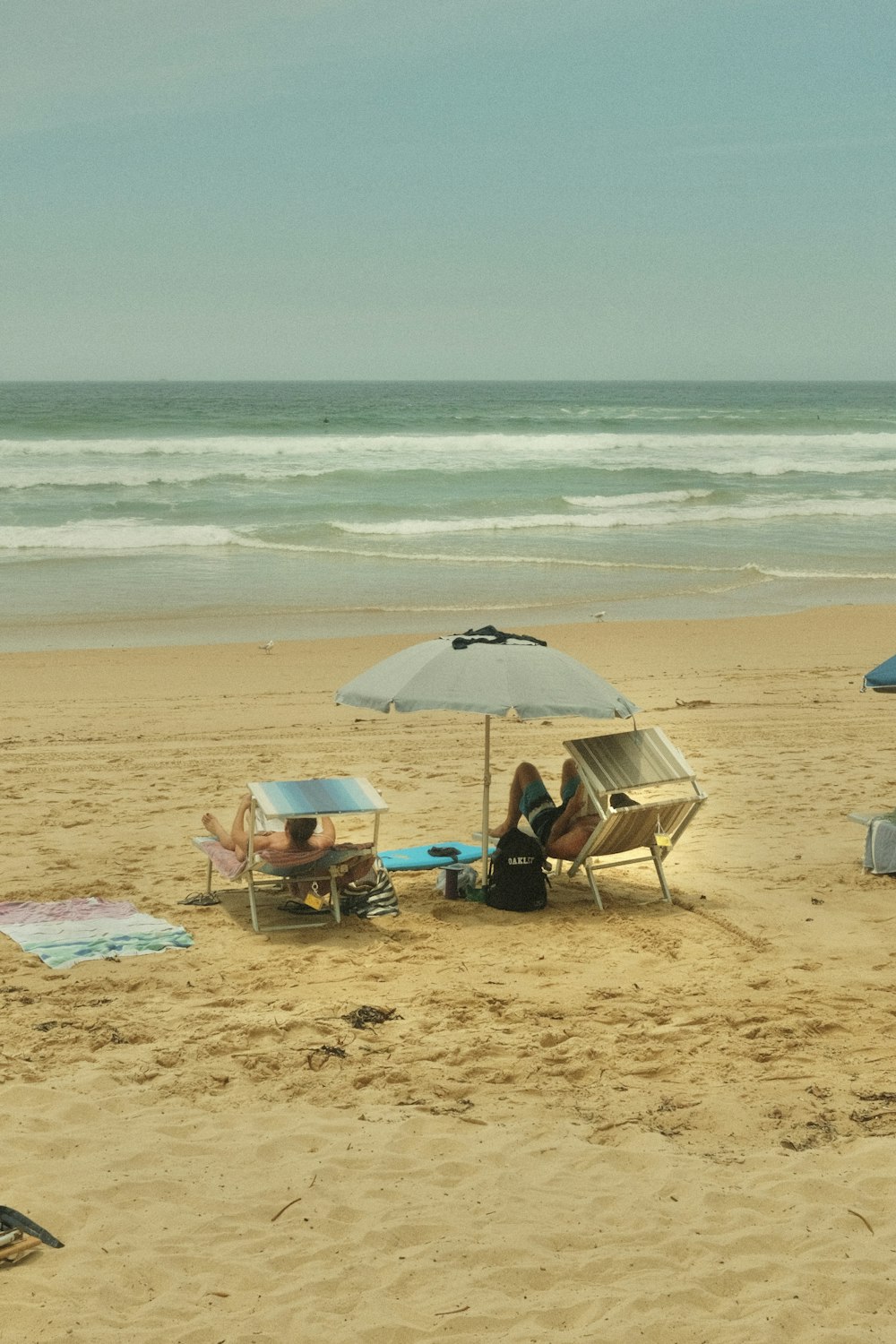 해변에서 우산 아래 앉아있는 두 사람