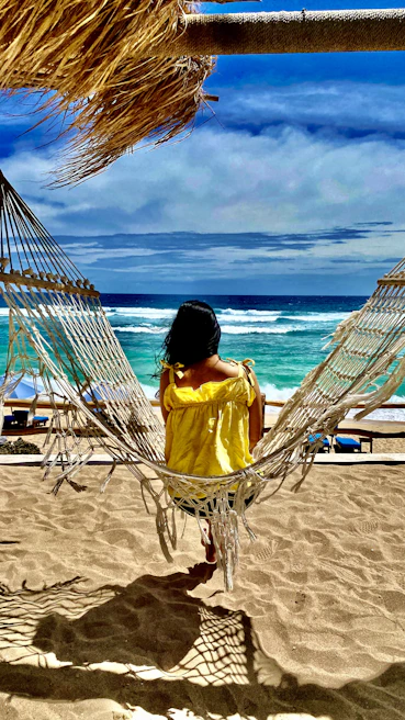 a woman sitting in a hammock on the beach