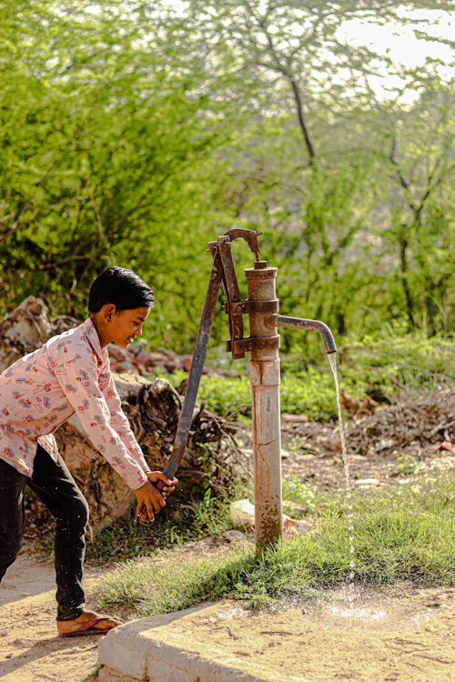 A boy pumping water among green plants
