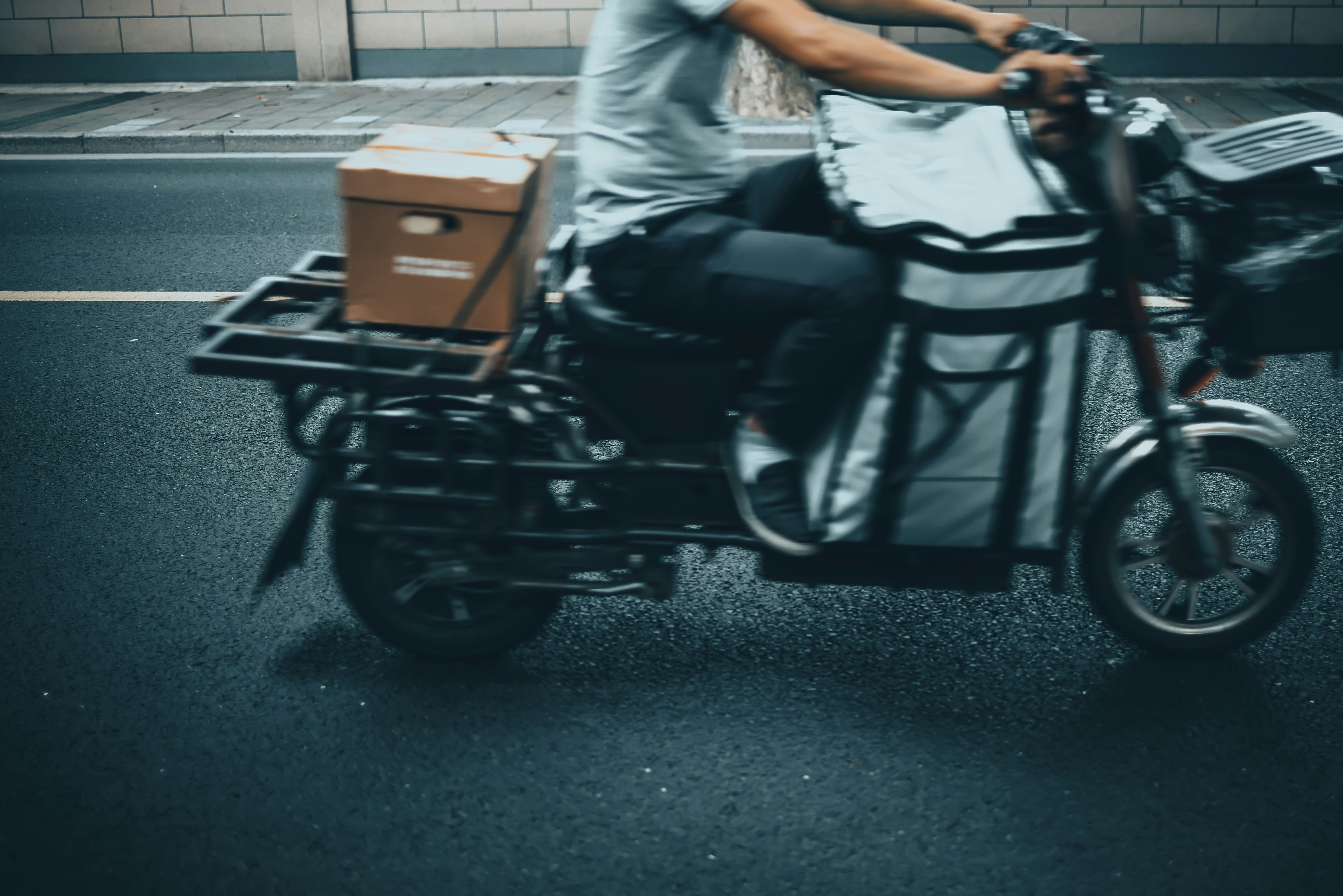 Operación de distribución urbana con repartidor cargando caja en calle, entorno urbano oscuro y sombreado, iluminación de calle