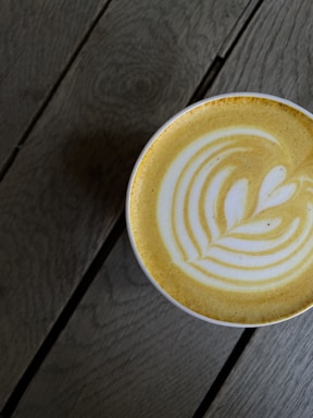 Close-up of a steaming cup of creamy coffee with latte art on a rustic wooden table