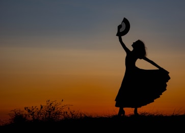 a silhouette of a woman holding a hat