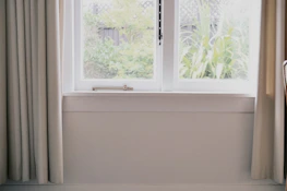 A bright living room featuring large, newly installed glass windows overlooking a garden.