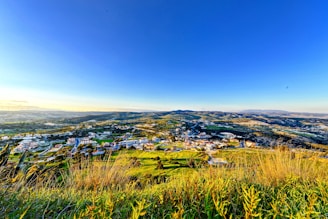 A panoramic view from a hilltop overlooking a patchwork of green fields and distant villages.