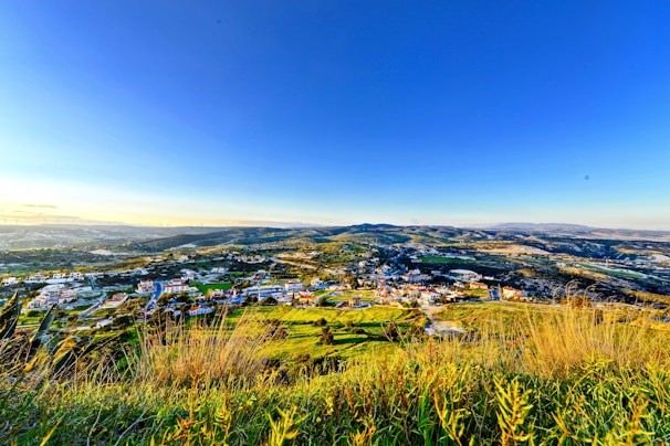 A panoramic view from a hilltop overlooking a patchwork of green fields and distant villages.