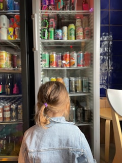 a little girl sitting in front of a refrigerator filled with drinks