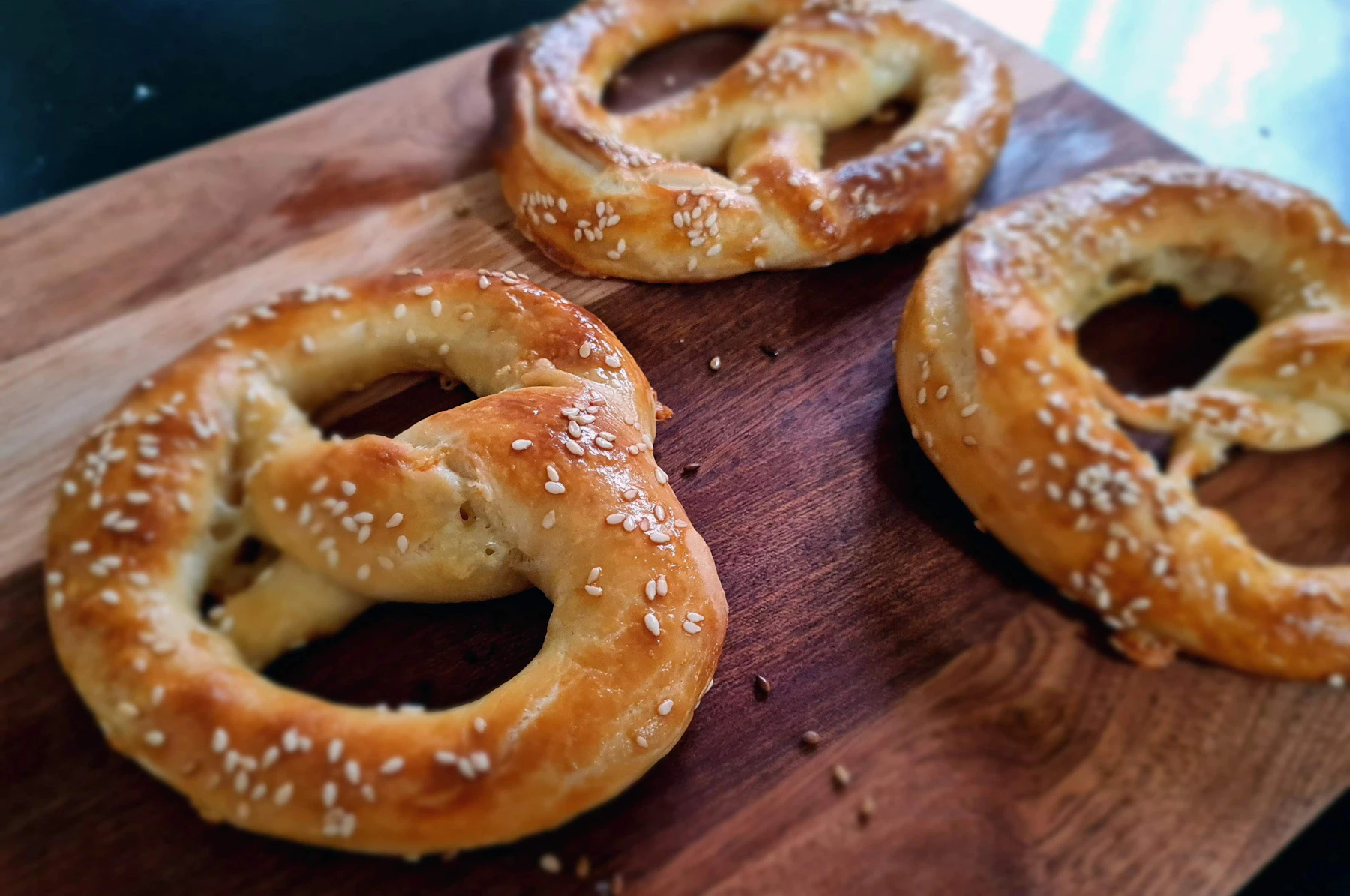 Three salted homemade soft pretzels on a wooden cutting board