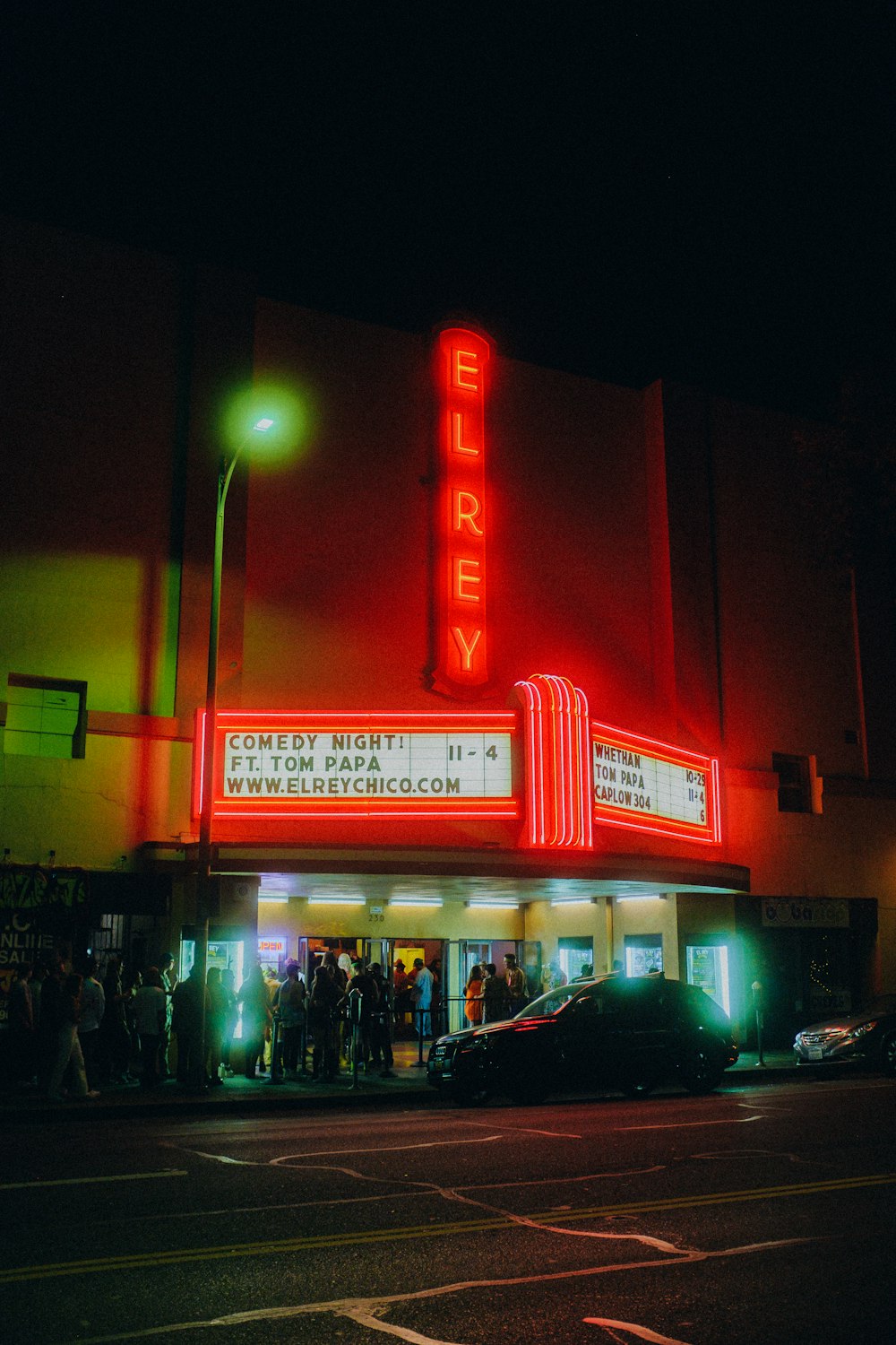 a movie theater with people standing outside at night