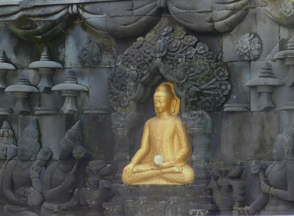 a golden buddha statue sitting in front of a stone wall