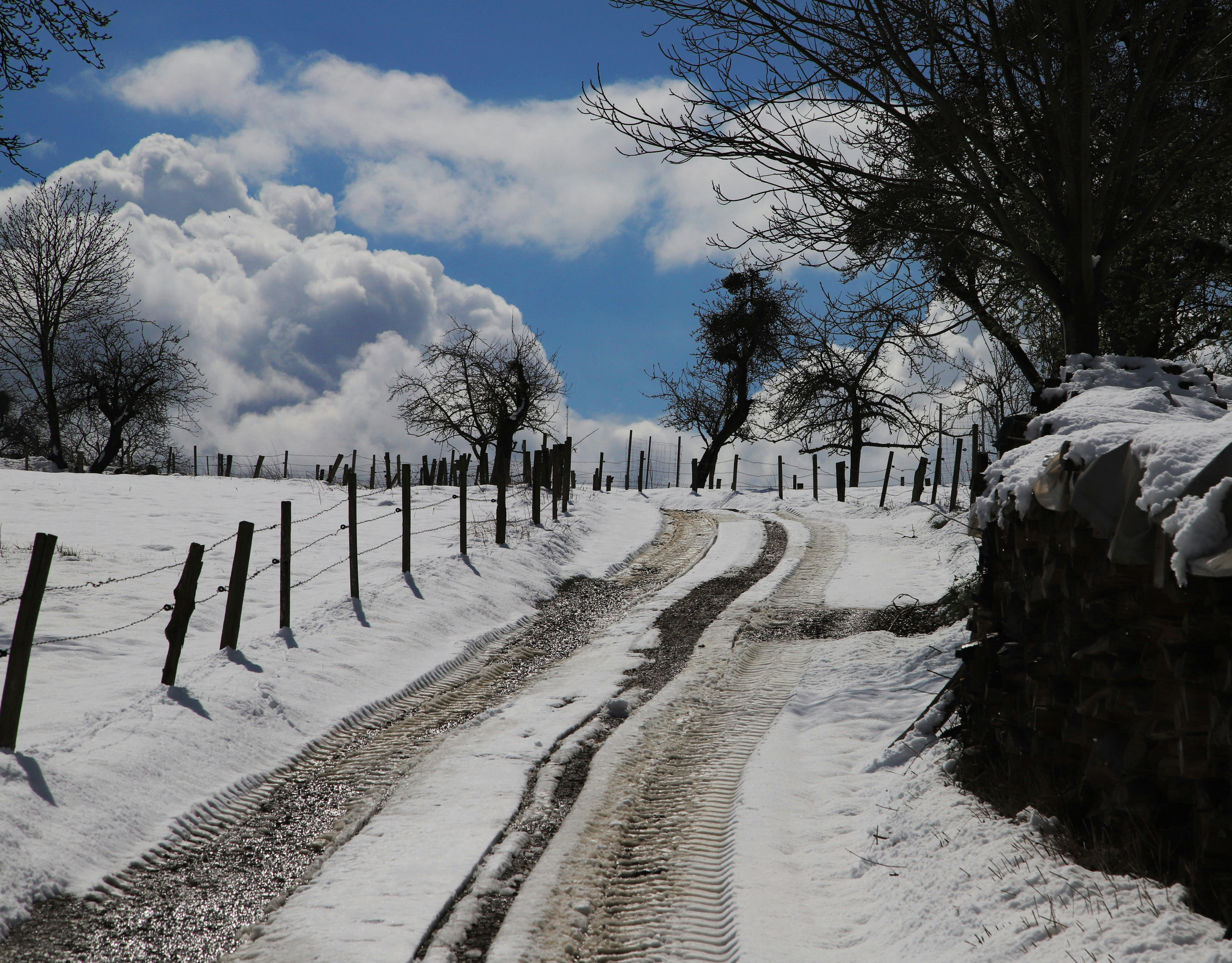 a dirt road with a fence and snow on the ground