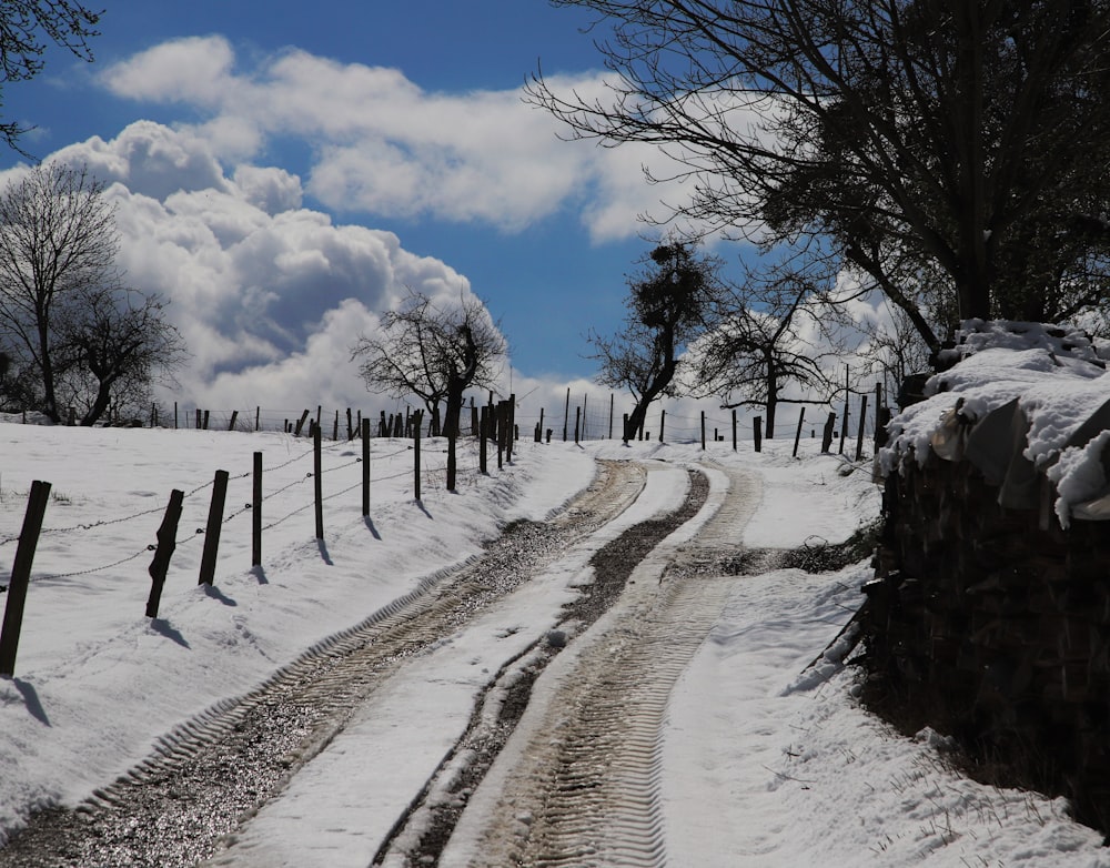 a dirt road with a fence and snow on the ground