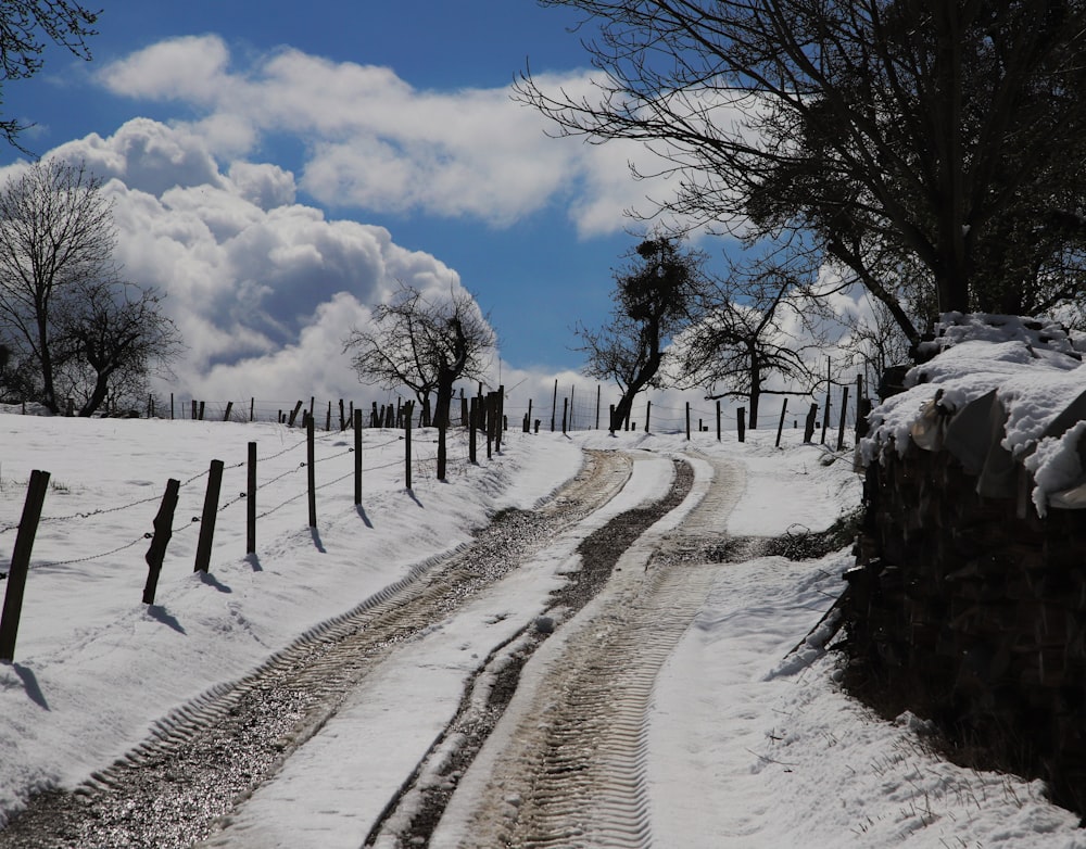 Un camino de tierra con una valla y nieve en el suelo