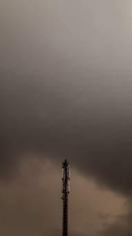 A tall telecommunications tower stands prominently against a backdrop of heavy, dark clouds. The sky has a tumultuous look, suggesting an impending storm or bad weather.