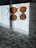 A pair of round, brown-tinted sunglasses rests on a reflective, speckled granite surface. The reflection of the sunglasses is visible on the surface, and there is a soft light coming through the blinds, casting subtle shadows.