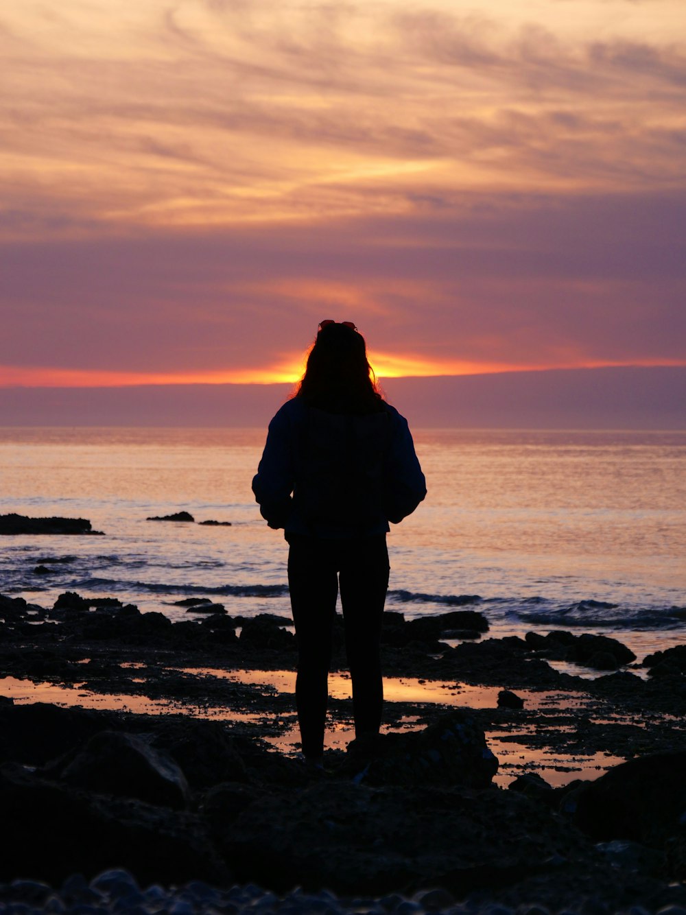 a person standing on a rocky beach at sunset