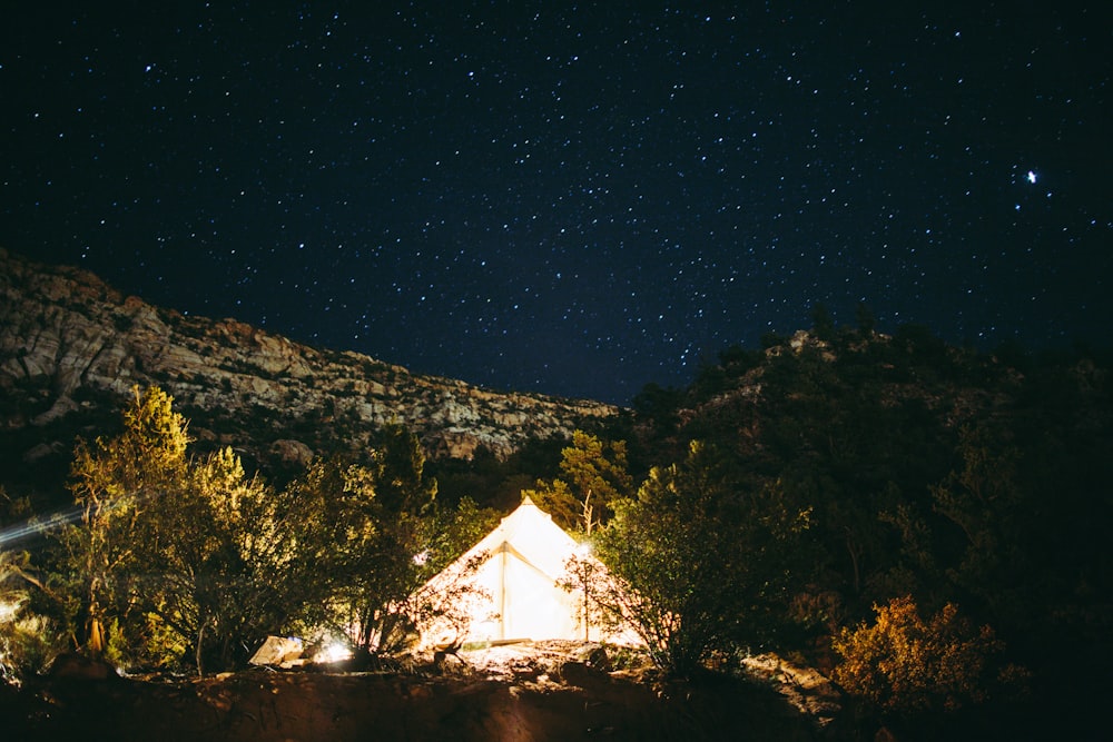 a tent is lit up at night in the mountains